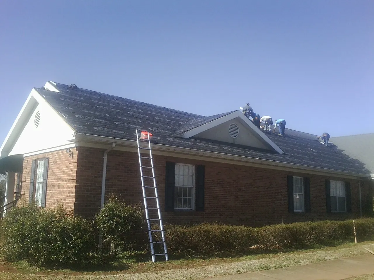 Crew tearing shingles off a brick ranch roof with a ladder set — Metal Roof Repair work by our crew in Mazon
