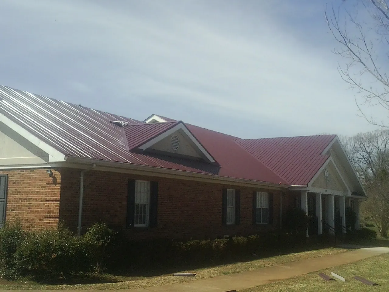 Red metal roof with gabled entries on a long brick building, from a Hail Damage Roof Repair job in Mazon