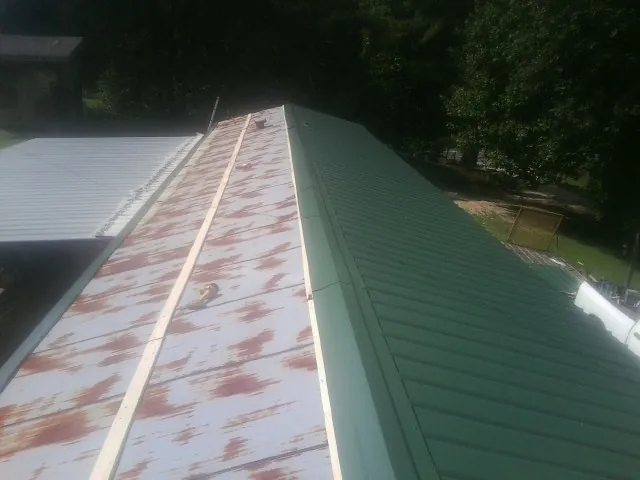 Old rusted panels beside newly installed green metal roofing — Wind Damage Roof Repair by Roofing Brothers in Mazon
