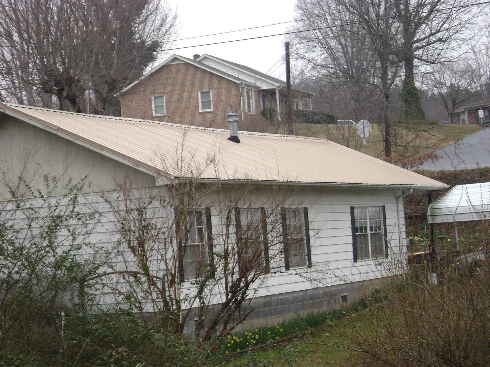 Tan metal roof on a white sided house set into a hillside — Commercial Roofing by Roofing Brothers in Mazon