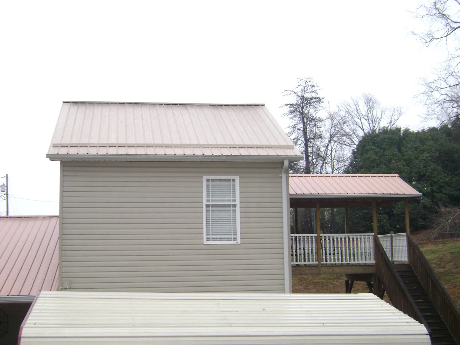 Tan metal roofs on a two story addition and attached porch, from a Roof Replacement job in Mazon
